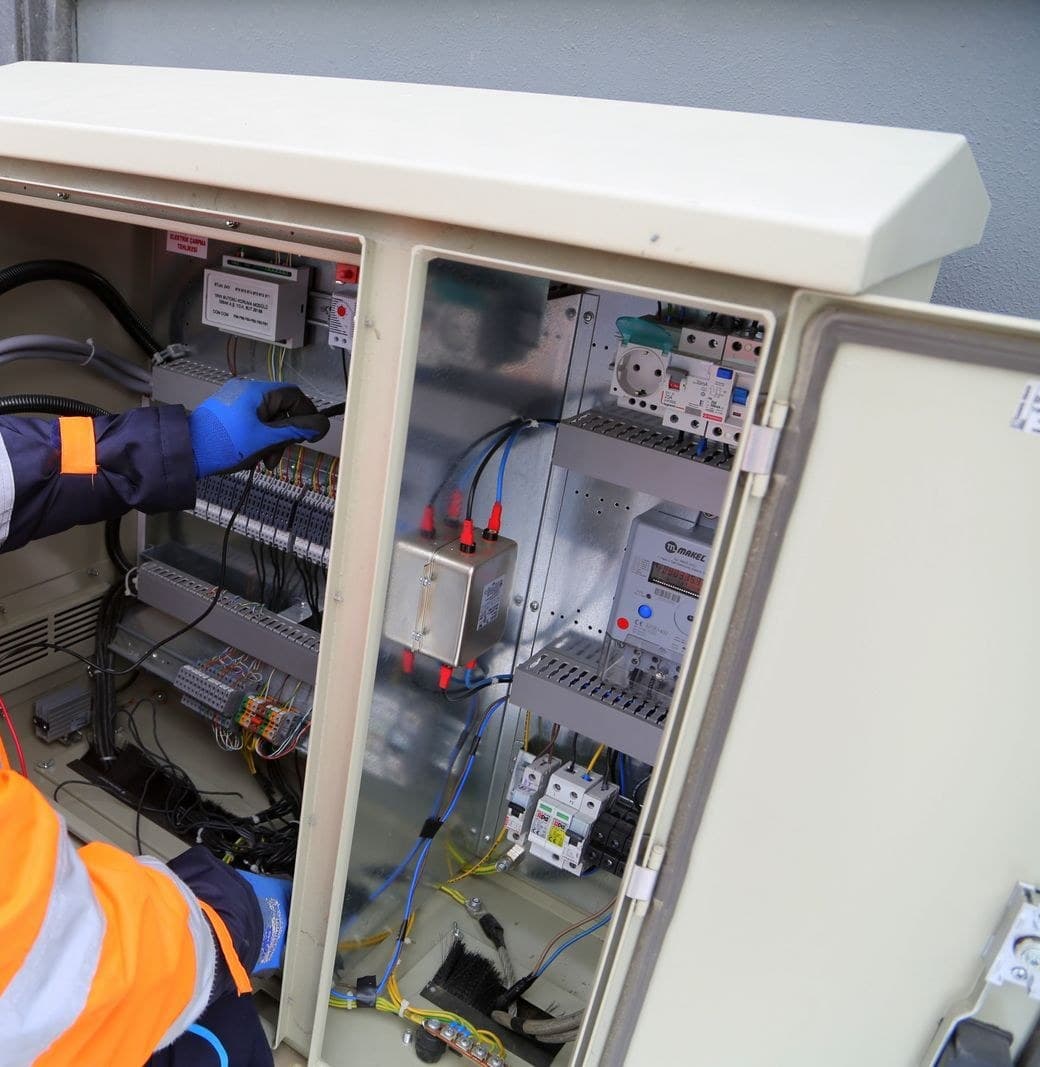 A gloved hand working inside an open electrical control cabinet