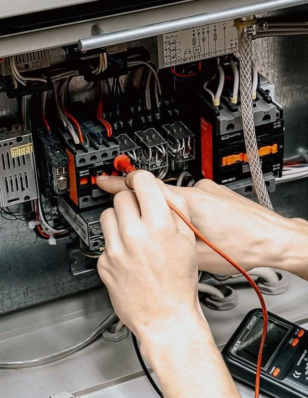 An electrician testing connections in an open panel with a multimeter