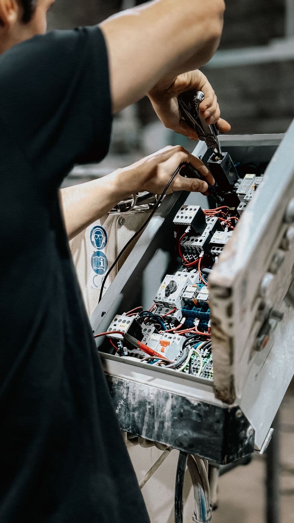 Hands wiring components inside an open electrical control cabinet