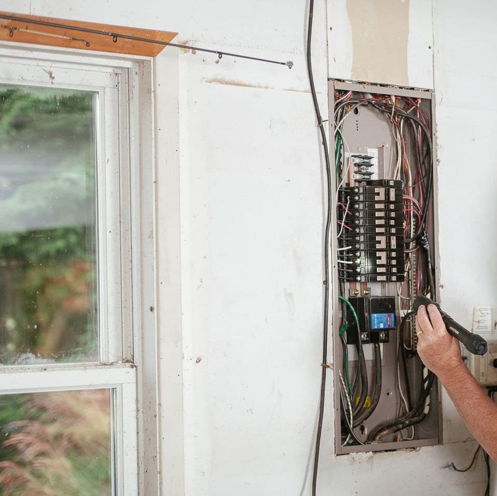 A residential service panel with wiring, and a hand holding a tester beside it