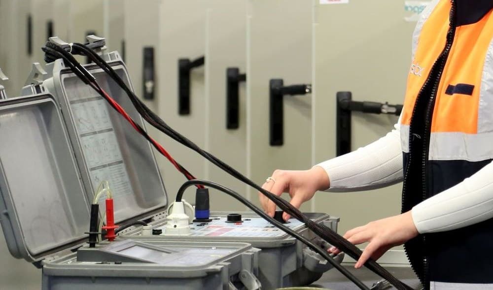 A technician in a high-visibility vest operating portable electrical test equipment